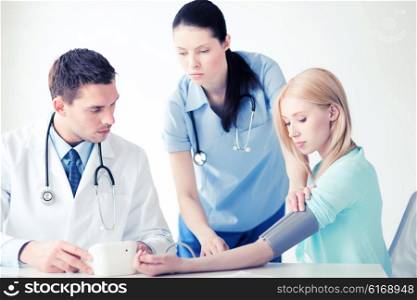 healthcare and medical concept - doctor and nurse with patient measuring blood pressure in hospital. doctor and patient in hospital