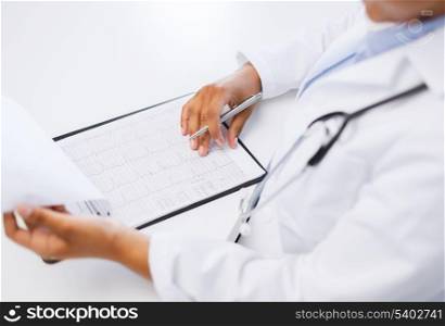 healthcare and medical concept - female doctor hands studies cardiogram holding pen