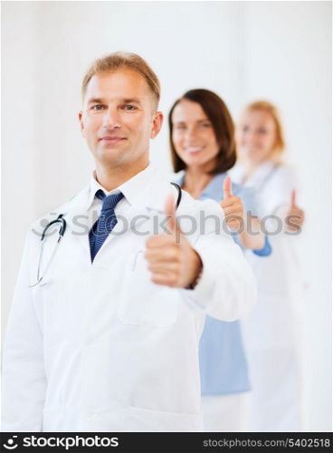 healthcare and medical concept - male doctor with stethoscope and colleagues showing thumbs up