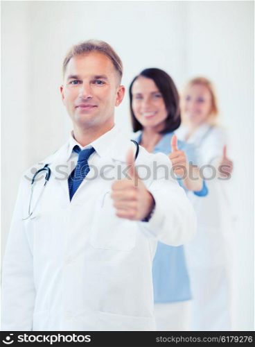 healthcare and medical concept - male doctor with stethoscope and colleagues showing thumbs up. doctor with stethoscope and colleagues