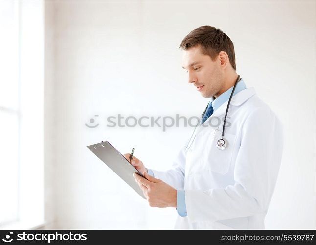 healthcare and medical concept - smiling male doctor with stethoscope and clipboard in hospital
