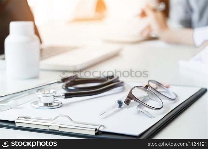 Healthcare and Medical concept, View of stethoscope and equipment on foreground table with patient listening intently to a female doctor as they discuss paperwork together in a consultation.