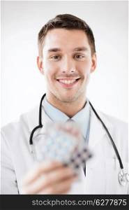 healthcare and medical concept - young male doctor with packs of pills