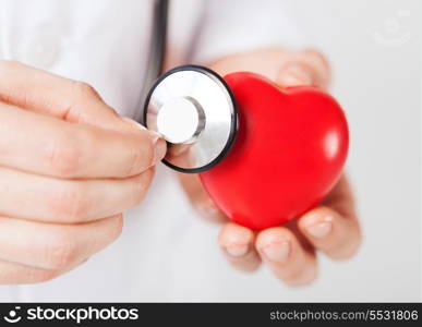 healthcare and medicine concept - close up of male hands holding red heart and stethoscope