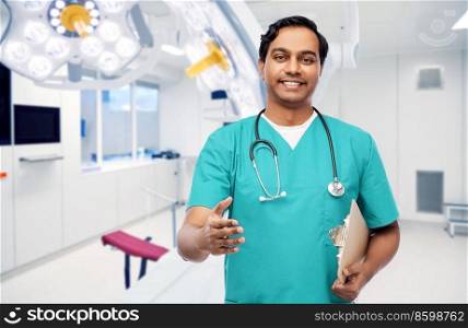 healthcare and medicine concept - happy smiling doctor, surgeon or male nurse in blue uniform with clipboard and stethoscope giving hand for handshake over surgery ward at hospital on background. male doctor giving hand for handshake at clinic