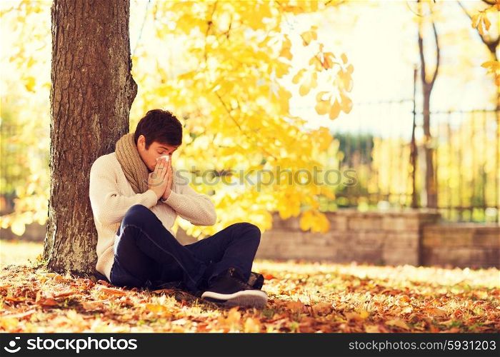 healthcare and medicine concept - ill man with paper tissue in autumn park. ill man with paper tissue in autumn park