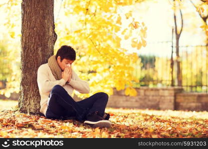 healthcare and medicine concept - ill man with paper tissue in autumn park. ill man with paper tissue in autumn park