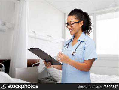 healthcare and medicine concept - smiling female doctor or nurse in eyeglasses with stethoscope and clipboard over hospital ward background. smiling female doctor or nurse at hospital ward