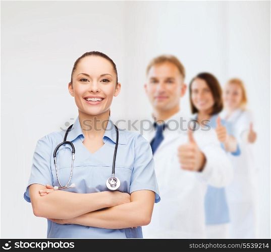 healthcare and medicine concept - smiling female doctor or nurse with stethoscope and team on the back showing thumbs up