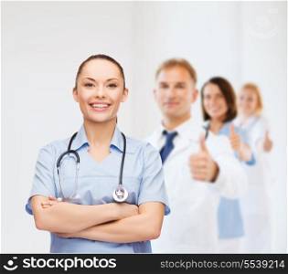 healthcare and medicine concept - smiling female doctor or nurse with stethoscope and team on the back showing thumbs up