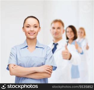 healthcare and medicine concept - smiling female doctor or nurse with team on the back showing thumbs up