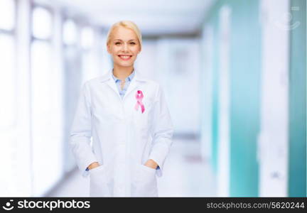 healthcare and medicine concept - smiling female doctor with pink cancer awareness ribbon over hospital background