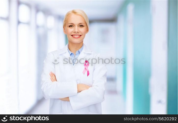 healthcare and medicine concept - smiling female doctor with pink cancer awareness ribbon over hospital background