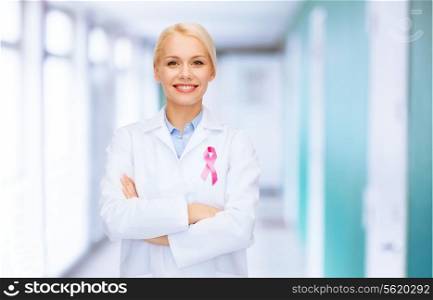 healthcare and medicine concept - smiling female doctor with pink cancer awareness ribbon over hospital background