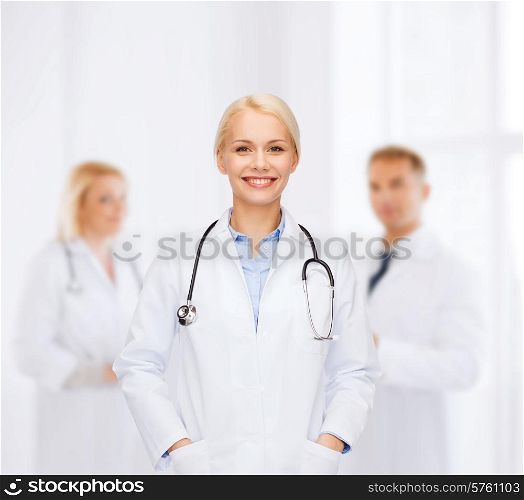 healthcare and medicine concept - smiling female doctor with stethoscope over background with group of medics in hospital