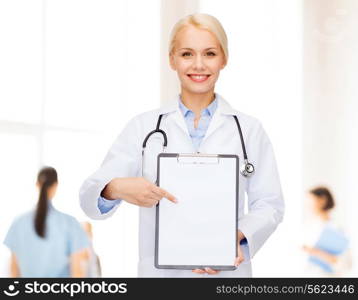 healthcare and medicine concept - smiling female doctor with stethoscope pointing finger to clipboard and blank page