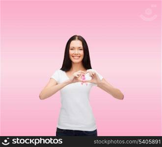 healthcare and medicine concept - smiling woman in blank white t-shirt with pink breast cancer awareness ribbon showing heart shape