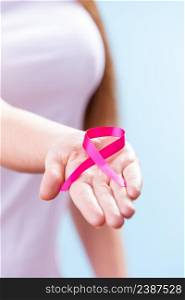 Healthcare and medicine concept - woman showing pink breast cancer awareness ribbon on hand, closeup on blue. Woman with breast cancer awareness ribbon on hand