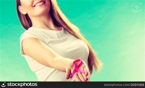 Healthcare and medicine concept - woman showing pink breast cancer awareness ribbon on hands, against green teal. Woman with breast cancer awareness ribbon on hands