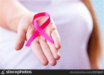 Healthcare and medicine concept - woman showing pink breast cancer awareness ribbon on hand, closeup. Woman with breast cancer awareness ribbon on hand