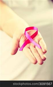 Healthcare and medicine concept - woman showing pink breast cancer awareness ribbon on hand, closeup. Woman with breast cancer awareness ribbon on hand