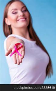 Healthcare and medicine concept - woman showing pink breast cancer awareness ribbon on hands, against blue. Woman with breast cancer awareness ribbon on hands