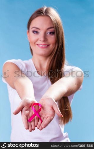 Healthcare and medicine concept - woman showing pink breast cancer awareness ribbon on hands, against blue. Woman with breast cancer awareness ribbon on hands