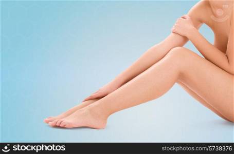 healthcare, beauty and people concept - beautiful woman touching her bare legs over blue background