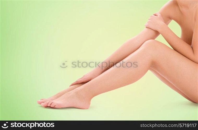 healthcare, beauty and people concept - beautiful woman touching her bare legs over green background