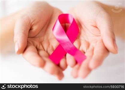 healthcare, charity, people and medicine concept - close up of woman cupped hands holding pink cancer awareness ribbon