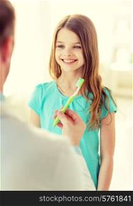 healthcare, child and medicine concept - male doctor giving toothbrush to smiling little girl