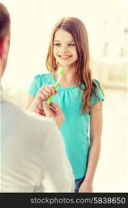 healthcare, child and medicine concept - male doctor giving toothbrush to smiling little girl