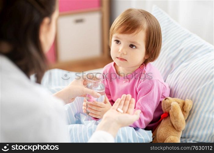 healthcare, children and people concept - doctor giving medicine to little sick african american girl in bed at home. doctor giving medicine to sick girl in bed at home