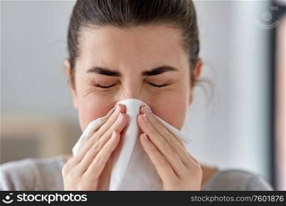 healthcare, cold, allergy and people concept - close up of sick woman blowing her runny nose in paper tissue at home. sick woman blowing nose in paper tissue at home
