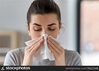 healthcare, cold, allergy and people concept - close up of sick woman blowing her runny nose in paper tissue at home. sick woman blowing nose in paper tissue at home