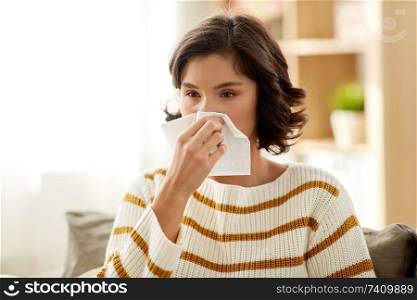healthcare, cold, allergy and people concept - sick woman blowing her runny nose in paper tissue at home. sick woman blowing nose in paper tissue at home
