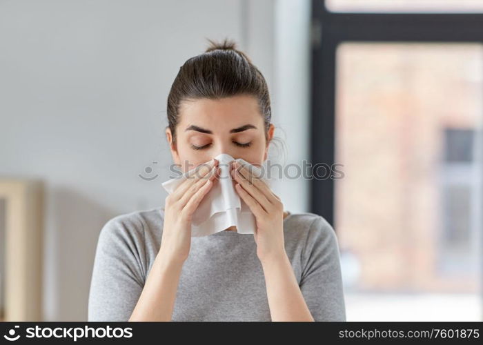 healthcare, cold, allergy and people concept - sick woman blowing her runny nose in paper tissue at home. sick woman blowing nose in paper tissue at home