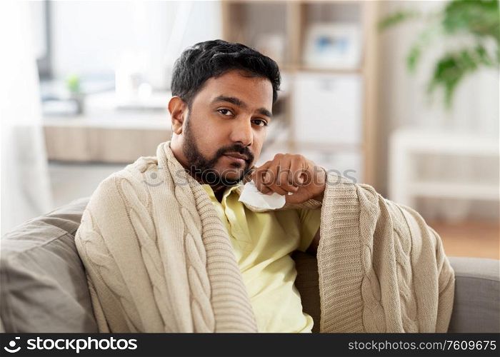 healthcare, cold, hygiene and people concept - sick indian man in blanket with paper tissue at home. sick man in blanket with paper tissue at home