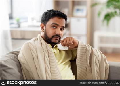 healthcare, cold, hygiene and people concept - sick indian man in blanket with paper tissue at home. sick man in blanket with paper tissue at home