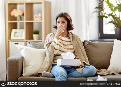 healthcare, cold, hygiene and people concept - sick woman blowing her runny nose in paper tissue at home. sick woman blowing nose in paper tissue at home