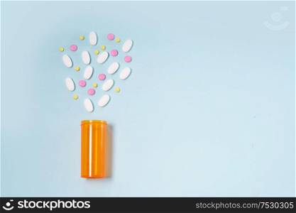 Healthcare concept - orange bottle with scattered pills on blue background with copy space. Healthcare concept on blue