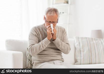 healthcare, flu, hygiene and people concept - sick senior man with paper wipe blowing his nose at home. sick senior man with paper wipe blowing his nose