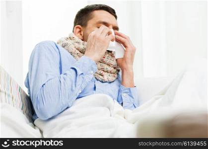 healthcare, flu, people, rhinitis and medicine concept - close up of ill man blowing his nose with paper napkin at home