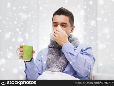 healthcare, flu, people, rhinitis and medicine concept - ill man blowing his nose with paper napkin and drinking tea at home over snow effect