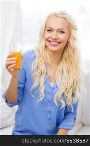 healthcare, food, home and happiness concept - smiling young woman with glass of juice having breakfast at home