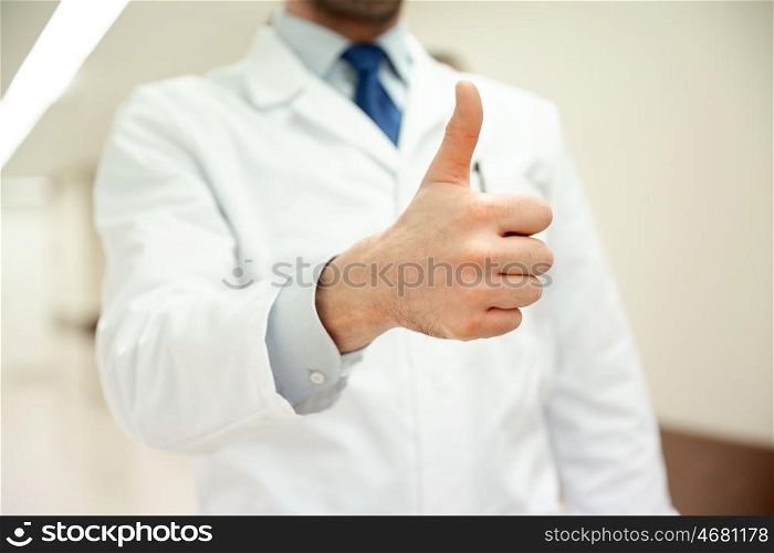 healthcare, gesture, people and medicine concept - close up of medic or doctor at hospital corridor showing thumbs up
