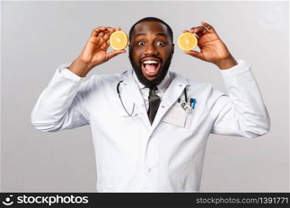 Healthcare, healthy diet and disease concept. Excited handsome african-american doctor in white coat, showing pieces of oranges and smiling amused, advice eat more food consist vitamin c, fruits.. Healthcare, healthy diet and disease concept. Excited handsome african-american doctor in white coat, showing pieces of oranges and smiling amused, advice eat more food consist vitamin c, fruits