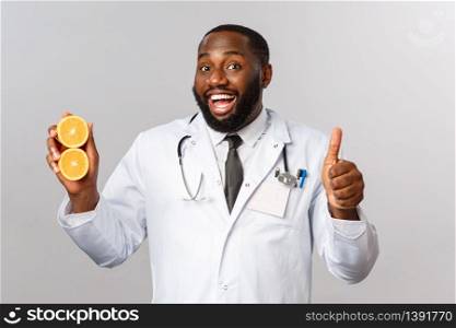 Healthcare, healthy diet and disease concept. Handsome african-american bearded doctor, physician or diatologist recommend eat fruits, showing oranges, avoid junk food, smile and thumb-up.. Healthcare, healthy diet and disease concept. Handsome african-american bearded doctor, physician or diatologist recommend eat fruits, showing oranges, avoid junk food, smile and thumb-up