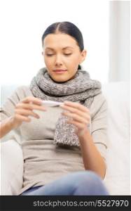 healthcare, home and medicine concept - ill woman with flu at home looking at thermometer