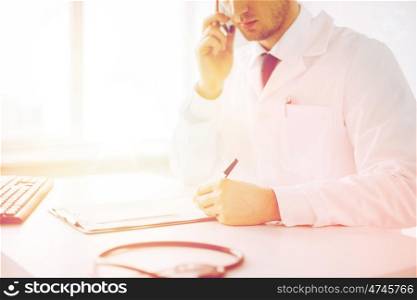 healthcare, hospital and medical concept - male doctor writing prescription paper and capsules